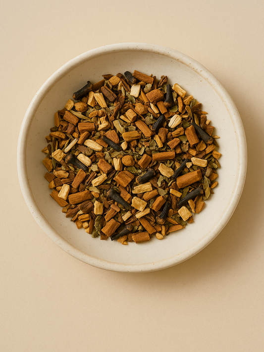Overhead view of dried Awaken Tea herbs in a ceramic bowl, featuring roasted dandelion root, chicory, cinnamon, and tulsi in a warm, earthy mix.