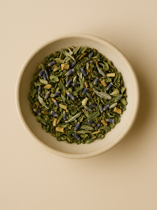 Overhead view of dried Bliss Tea herbs in a ceramic bowl, featuring nettle leaves and lavender buds for luteal phase support.