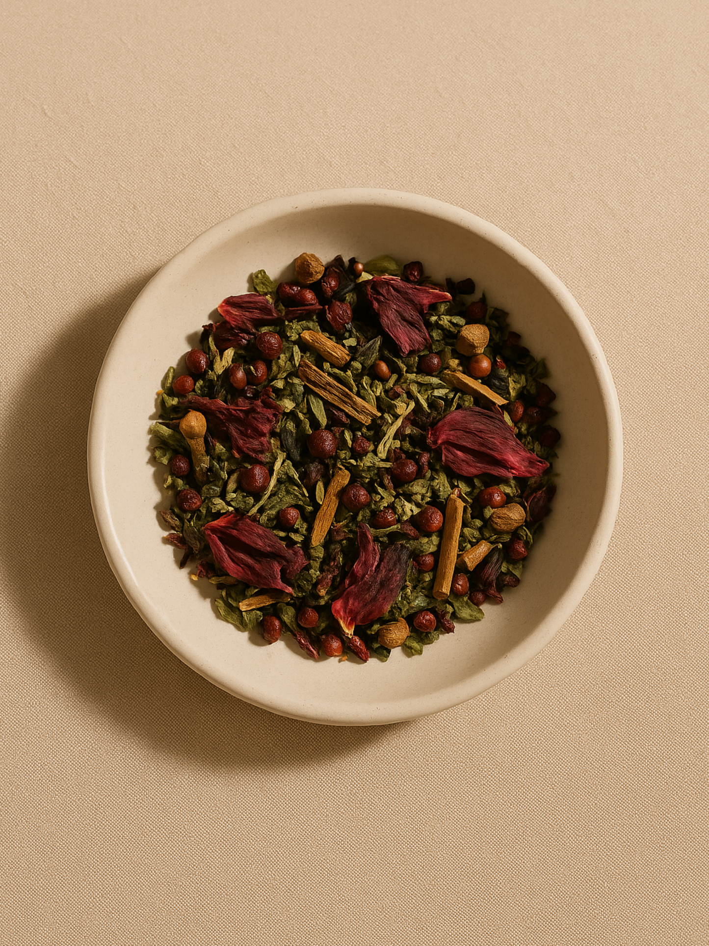 Overhead view of loose Flow Tea herbs in a ceramic bowl, showing hibiscus petals, cinnamon bark, and schisandra berries and nettle leaves on a soft neutral background.