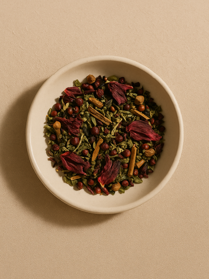 Overhead view of loose Flow Tea herbs in a ceramic bowl, showing hibiscus petals, cinnamon bark, and schisandra berries and nettle leaves on a soft neutral background.